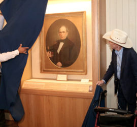A Ranger pulling back a blue curtain to reveal a framed circular portrait in an exhibit case.
