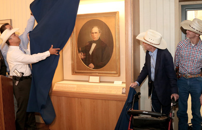 A Ranger pulling back a blue curtain to reveal a framed circular portrait in an exhibit case.