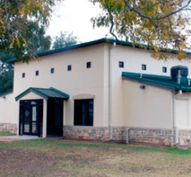 A white building with a green roof and a tan rock rim along the bottom.