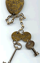 A brass key ring with two keys on it. The key ring says "Texas Rangers Sargent of Arms Co. B" and one key is labeled "Arms" and the other "Ammo".