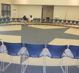 A large circle of chairs set up in a room with a few people in it.
