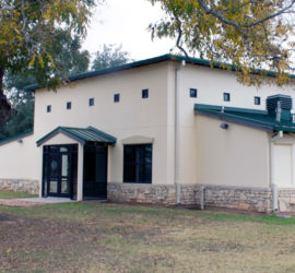 A white building with a green roof and a tan rock rim along the bottom.