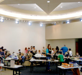 A group of kids and adults working on different activity tables in a round classroom space.