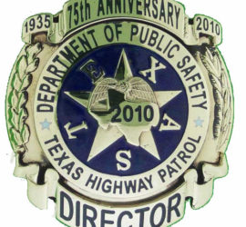 A silver circle badge with the words "1935 75th Anniversary 2010" on a ribbon shape across the top and the word "Director" on a ribbon shape along the bottom. Along the sides are two leafy branches. In the middle is an alteration of the original circular DPS badge with the words "Department of Public Safety" and "Texas Highway Patrol" along the outside of the circle separated by two stars. In the middle is a star with the letters that spell out "Texas" alternating with the star points on a dark blue background. In the center of the star is the shape of Texas with an eagle on top and the year "2010" in the middle.
