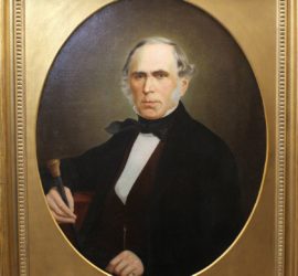 A framed circular portrait of an older man in a dark suit holding a cane.