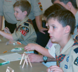 Boy scouts and adults in uniform working on a craft project.