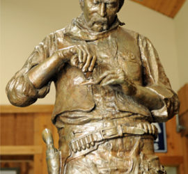 A close up on a larger than life bronze statue of a Ranger rolling a cigarette.