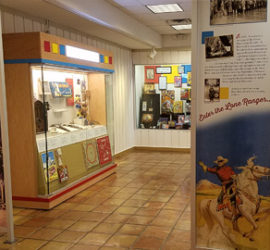 A brightly colored exhibit gallery with three cases visible and two large printed floor to ceiling panels.