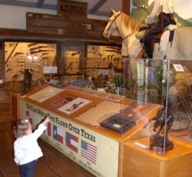 A small child in a white shirt pointing up at an exhibit of a mannequin on a horse.