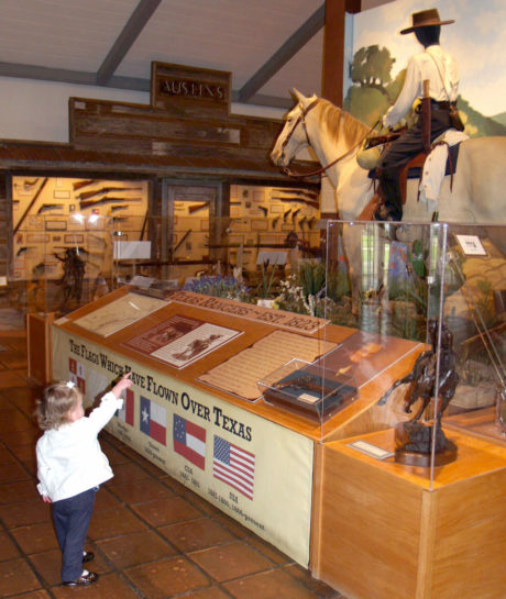 A small child in a white shirt pointing up at an exhibit of a mannequin on a horse.