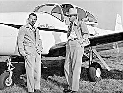 Two men in suits, one with a cowboy hat, leaning against a small plane outside. The plane has "Texas Ranger" written on it.