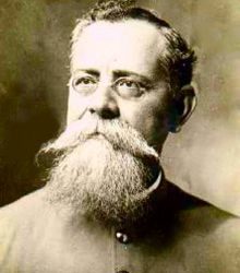 A black and white head shot of a man with glasses a beard and a large mustache.