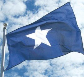 A solid blue flag with a white star in the center flying against a blue cloudy sky.
