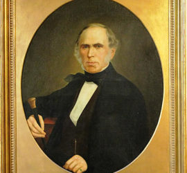 A framed circular portrait of an older man in a dark suit holding a cane.