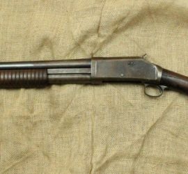 A shotgun with a wooden stock with the butt covered by a suede cover.