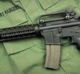 A dark grey assault rifle against a green uniform shirt with "Texas Rangers" embroidered above the right pocket.
