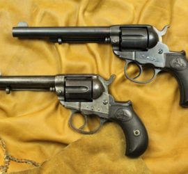 Two dark metal revolver pistols with a carved horse in a circle on the grips.