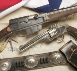One rifle, one pistol, a pocket knife, and a black gunbelt with silver accents arrange across an older map. The edge of the Texas flag is visible in the top left corner.