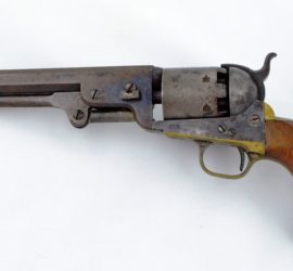 A pistol with wooden grips and a brass trigger and trigger guard.