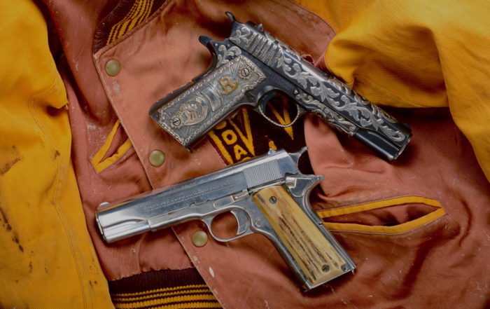 One simply decorated automatic pistol with a wooden or bone grip and one heavily decorative pistol on top of an orange letterman jacket.