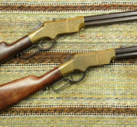 Two repeating rifles with wooden butts and brass receivers. One gun's receiver has engraving on it. Both guns rest on a multicolored saddle blanket.