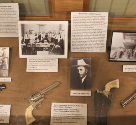 An exhibit case with photographs, labels, and various pistols.