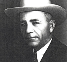 A man in a dark suit with a dark tie in a white cowboy hat.