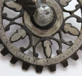 A dark and light silver dully spiked wheel with simple fleur de lis shapes as the spokes.
