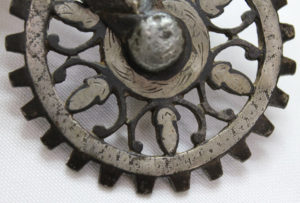 A dark and light silver dully spiked wheel with simple fleur de lis shapes as the spokes.