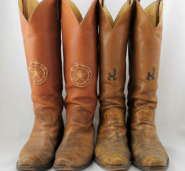 Two pair of worn brown leather cowboy boots. One pair has the circle star badge symbol and the other has a cattle brand on them.