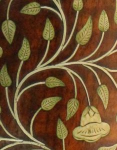 A close up of leaf and flower inlay on a wooden surface.