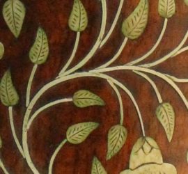 A close up of leaf and flower inlay on a wooden surface.