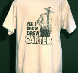 A white t-shirt with the words "Yes I Know Drew Carter" printed on it and a drawn image of a man in a cowboy hat, dress shirt and tie, and a western gun belt.
