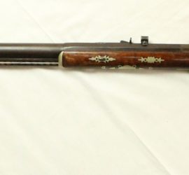 A percussion rifle with gold decorations and leaf and flower inlaid decorations along the butt of the firearm.
