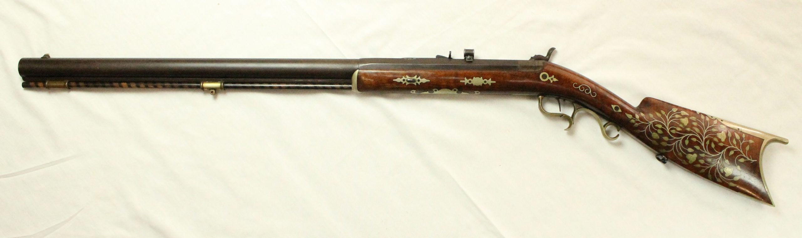 A percussion rifle with gold decorations and leaf and flower inlaid decorations along the butt of the firearm.