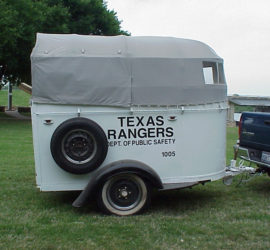 A white horse trailer with a grey canvas top attached to a blue pick up truck with the words "Texas Rangers Dept. of Public Safety 1005" on the trailer.