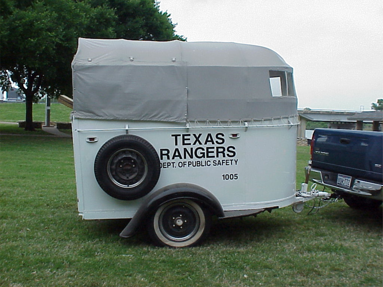 A white horse trailer with a grey canvas top attached to a blue pick up truck with the words "Texas Rangers Dept. of Public Safety 1005" on the trailer.