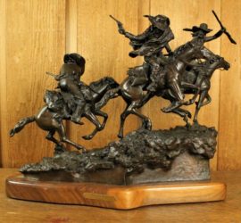 A small bronze statue of three cowboys mounted on running horses brandishing various weapons.