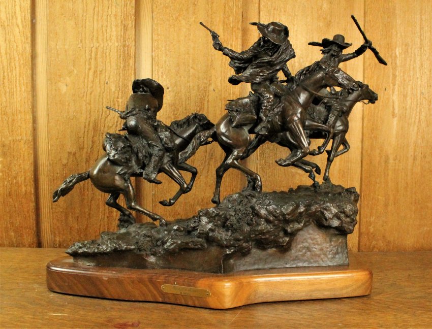 A small bronze statue of three cowboys mounted on running horses brandishing various weapons.