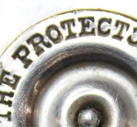 A zoomed in picture on a round metal circle that reads "The Protector"