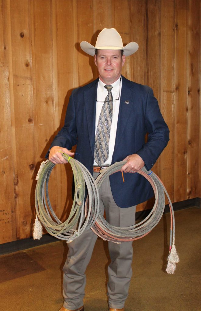 A man in a white hat, dark sport coat, and khaki slacks holds two lariats.