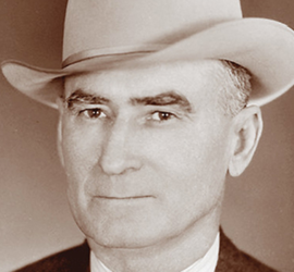 A head shot of a man in a light colored small brimmed hat.