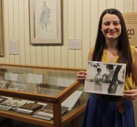 lady holding black and white photograph beside museum exhibits
