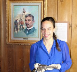 lady holding revolver in front of Aten painting