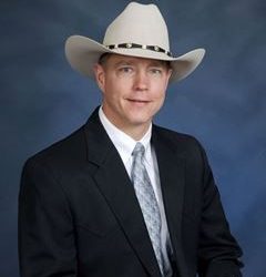 man in white cowboy hat and black suit on blue background