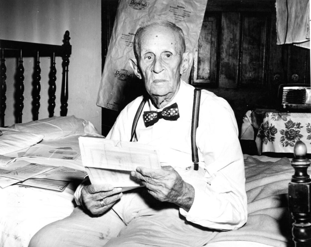 older man with bowtie reading on a bed