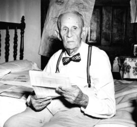 older man with bowtie reading on a bed