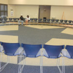 A large circle of chairs set up in a room with a few people in it.