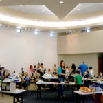 A group of kids and adults working on different activity tables in a round classroom space.