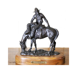 A small bronze sculpture of a cowboy on a horse. The cowboy is looking behind himself while the horse is grazing.